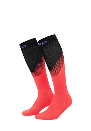 Paar knielange Sportsocken in leuchtendem Rot mit schwarzen strukturierten Oberteilen und lila Branding an den Bündchen, aufrecht und nebeneinander gezeigt.