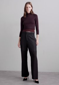 Pantalons larges noirs avec une texture lisse, associés à un col roulé ajusté en ribstop bordeaux, créant une silhouette épurée.