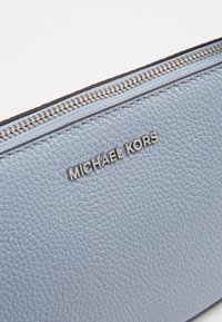Pochette en cuir bleu clair avec une surface texturée, des accessoires en métal argenté, et le logo "MICHAEL KORS" en relief à l'avant.