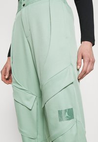 Mintgroene cargobroek met meerdere zakken, een geplooid ontwerp en een logopatch. Gemaakt van zachte stof met een gladde textuur.