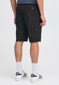 Shorts cargo noirs en coton, dotés de poches latérales, de coutures accentuées et d'une coupe décontractée, associés à des chaussettes blanches et des baskets.