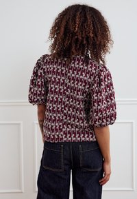 Burgundia värvi padjavarrukatega pluus, millel on lillene muster ja tekstuuriga kangas. Paaritatud tumedate teksapükstega, millel on kaks tagataskut.