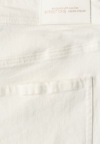 Tissu en denim blanc avec une poche arrière et une étiquette cousue indiquant "designed with passion STREET ONE - DENIM ATELIER".