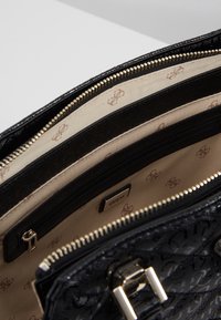 Sac à main noir à surface texturée, doté de ferrures dorées, de plusieurs compartiments et d'une doublure beige avec un motif logo répété.