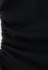 Gros plan d'un tissu côtelé noir avec une texture froncée ou plissée, montrant des plis et de fines lignes verticales.
