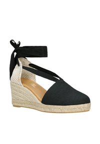 Black espadrille wedge shoe with a textured canvas upper, woven jute sole, and crisscross black ribbon straps. Features a patterned interior.