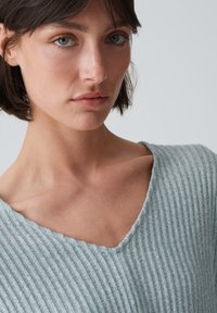 Hellgrauer gerippter Pullover mit V-Ausschnitt und weichem Material, der feine vertikale Linien und eine lockere Passform aufweist.