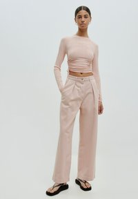 Roze geribbelde top met lange mouwen en een geplooide zijdetail, gecombineerd met lichtroze, hoge taille wijd-uitlopende broeken en zwarte slippers.