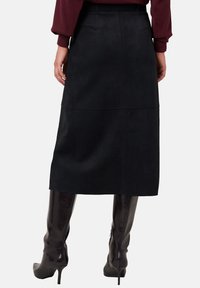 Woman wearing a black midi skirt, maroon sweater, and knee-high black leather heeled boots, standing with hands relaxed at sides.