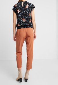 Svart blus med blommönster och korta ärmar, kombinerad med rostfärgade byxor. Stilren ögla i ryggen. Beiga ankelstövlar.