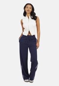 Witte geribde mouwloze top met een ritssluiting aan de voorkant, gecombineerd met marineblauwe wijde sweatpants met witte zijstrepen en een verstelbare tailleband.