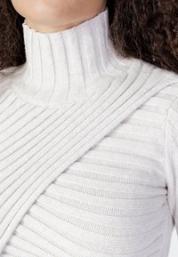 Maglione bianco a collo alto in maglia con dettagli a righe diagonali sul petto.
