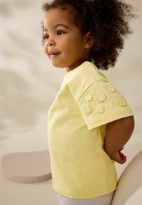 Gul bomulds T-shirt med korte ærmer, prydet med broderede blomsterdetaljer på skulderen, afslappet pasform og glat tekstur.