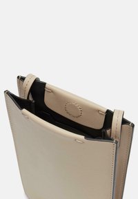 Beige Lederhandtasche mit schwarzen Akzenten, die eine strukturierte Form, einen offenen oberen Teil und eine kleine innere Tasche mit einem runden Druckknopfverschluss aufweist.