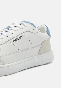 Zapatilla de cuero blanca con acentos de ante azul claro y beige, suela de goma texturizada y detalles perforados. Logotipo "Morato" en el lateral.