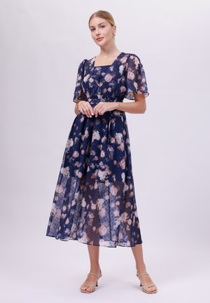 Navy floral maxi dress with sheer, short puff sleeves, square neckline, and pleated skirt featuring a polka dot pattern among the flowers.