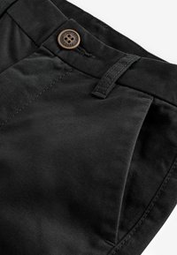 Pantalons en coton noir avec une texture lisse, dotés d'une fermeture à bouton et de poches avant angulaires. Les coutures sont visibles le long des bords.