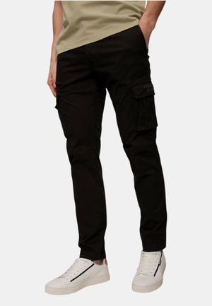 Pantaloni cargo neri in cotone con tasche laterali e vestibilità rilassata. Abbinati a sneaker bianche con una striscia nera.