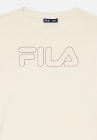 Beige bomulls t-shirt med en stor, subtil FILA-logotyp i en mörkare nyans, standard rundad halsringning med mjuk textur och korta ärmar.