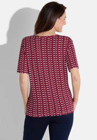 Haut à manches courtes avec un motif géométrique rouge, blanc et marine, fabriqué en tissu doux, avec un décolleté rond et une coupe décontractée.