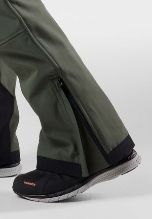 Green waterproof pants with zippers at the sides, paired with black Treksta shoes featuring a textured rubber sole and mesh upper.