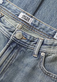 Vaaleansiniset farkut, joissa on haalistunut pinta, oranssit tikkaukset, metallinen nappi ja valkoinen etiketti, jossa on "JACK & JONES" -logo.