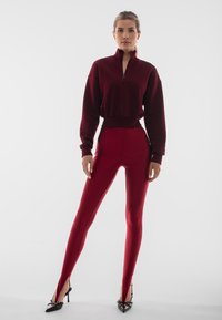 Bordo rozpinana bluza z długim rękawem, zestawiona z legginsami o wysokim stanie, obcisłymi i wykonanymi z gładkiego materiału. Posiada wysoki rozcięcie i akcenty w postaci obcasów.