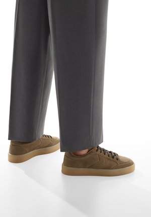 Sneaker in suede marrone con punta rotonda, lacci coordinati e suola in gomma beige; indossati con pantaloni grigi su misura.
