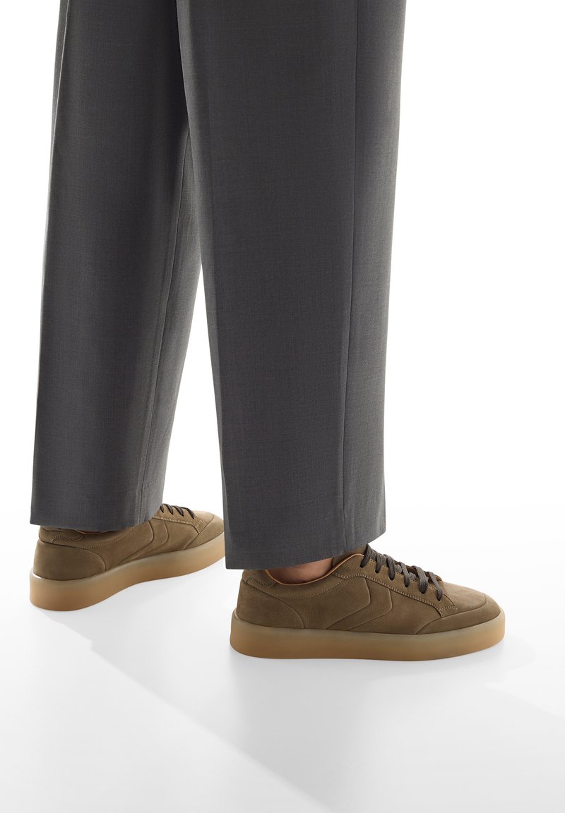 Sneaker in suede marrone con punta rotonda, lacci coordinati e suola in gomma beige; indossati con pantaloni grigi su misura.