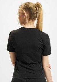 Melnas īsām piedurknēm t-krekls ar apaļu kakla izgriezumu, gludu tekstūru un pieguļošu griezumu, redzams no aizmugures ar izteiktām plecu detaļām.