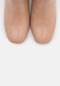 Stivali alla caviglia in pelle beige con una texture liscia, punta arrotondata e design minimalista. La superficie presenta leggere pieghe e una finitura opaca.