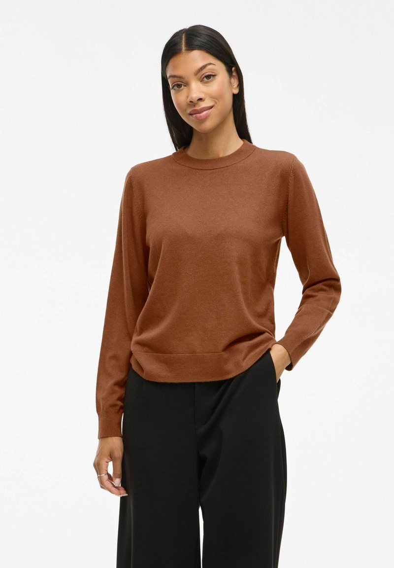 Un pull en tricot marron avec des manches longues et un col rond. Assorti à un pantalon noir à jambes larges, montrant une texture lisse et une coupe décontractée.