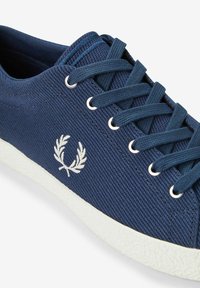 Zapatillas de lona azul marino con suela de goma blanca, que presentan un sistema de cierre con cordones y un logo de laurel bordado en el lateral. Superficie de tela texturizada.