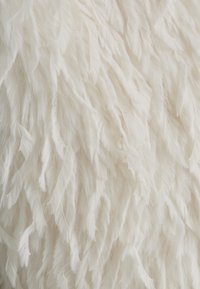 Weißer Kunstpelzstoff mit langen, weichen, strukturierten Fasern. Die Oberfläche weist ein gewelltes Muster mit subtil variierenden Längen auf.