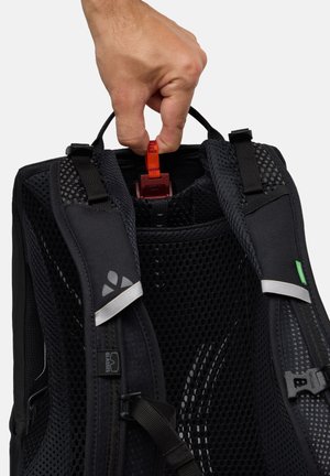 Zaino nero con texture a rete, spallacci regolabili e maniglia di presa. Nota linguetta rossa all'interno, dettagli argentati sugli spallacci.