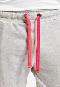 Light grey sweatpants feature metal eyelets and bright pink drawstrings. Fabric appears soft with a smooth texture.