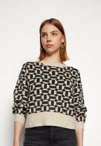 Maglione lavorato a maglia con un motivo geometrico nero e crema, dal design cropped, colletto rotondo e polsini e orlo a costine.