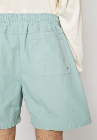 Ljust teal bomullsshorts med elastisk midja, med en bakficka och en len textur. Enkel design, inga synliga mönster.