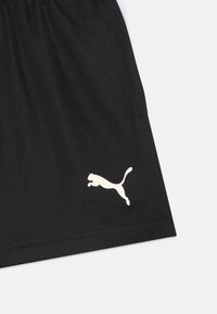 Fekete sportnadrág sima anyagból, elasztikus derékpánttal és egy fehér Puma logóval az alsó bal lábszáron.