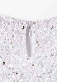 Witte paillettenjurk met een diepe V-hals, versierd met ronde, glanzende pailletten en een ritssluiting met een parelaccent bij de hals.