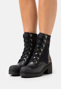 Bottines noires avec un mélange de cuir et de tissu. Présentent des œillets dorés, un bout rond et un talon épais avec des accents texturés.