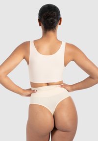 Jasno beżowy zestaw odzieży sportowej, składający się z dopasowanego topu na ramiączkach i wysokich majtek z przeźroczystą górną częścią. Gładka tekstura.