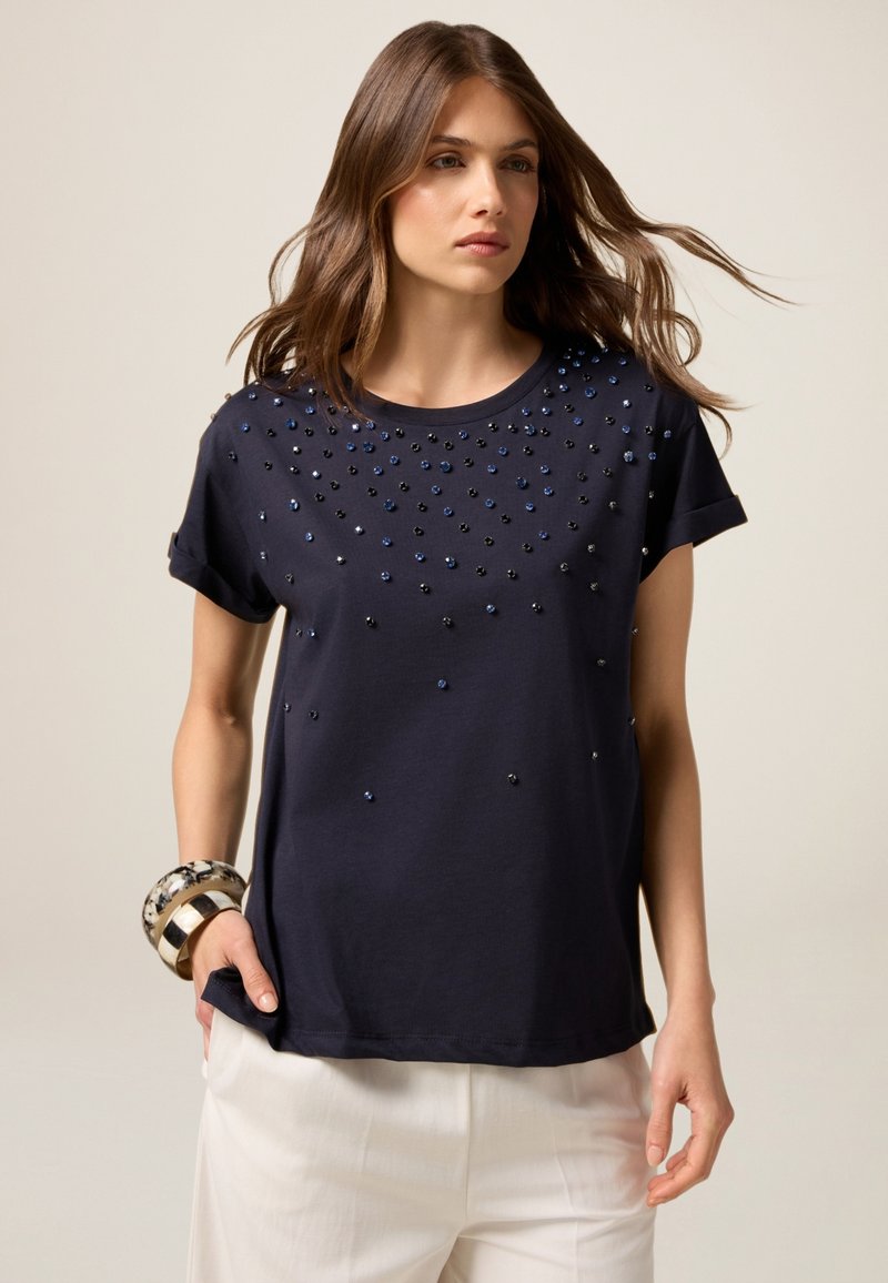 Camiseta de manga corta azul marino hecha de tela suave, con acentos de joyas negras y azules esparcidos en el escote y los hombros.