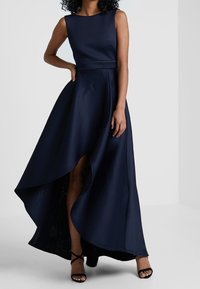 Abito senza maniche blu navy con corpino aderente e gonna asimmetrica, caratterizzato da uno spacco alto. Realizzato in tessuto liscio con una leggera lucentezza.