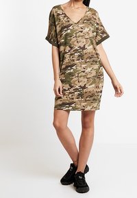 Robe à imprimé camouflage avec un décolleté en V et des manches courtes ; fabriquée en tissu doux ; présente une coupe ample et tombe juste au-dessus du genou.