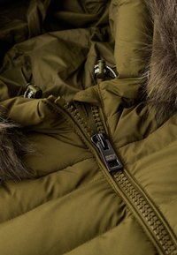 Olijfgroene pufferjack met een zichtbare gestepelde textuur. Voorzien van een plastic rits met "SUPERDRY" branding en nep-bontaccenten.
