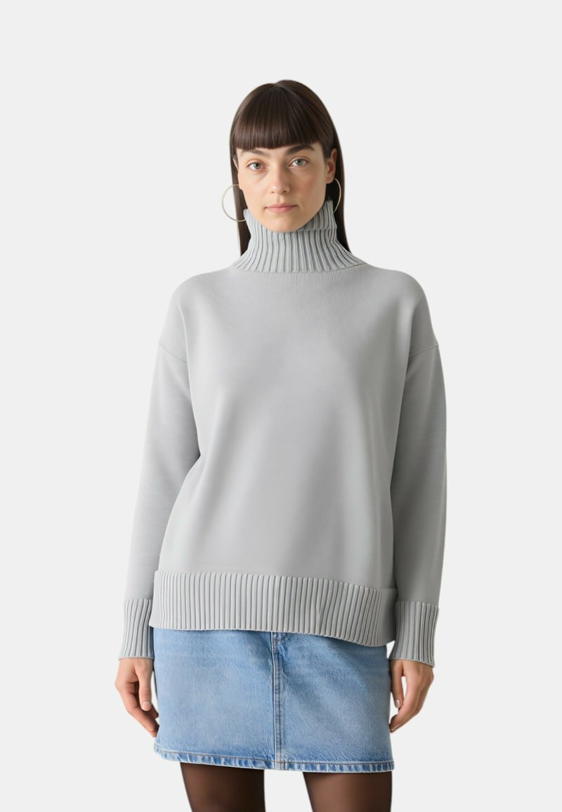 Maglione grigio chiaro con colletto alto a costine, polsini a costine e orlo dritto. Abbinato a una gonna di jeans per un look stratificato.