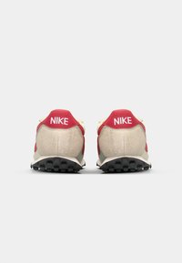 Red and beige Nike sneakers with a textured upper, cushioned heel, and black traction sole. Features prominent "Nike" branding on the heel.