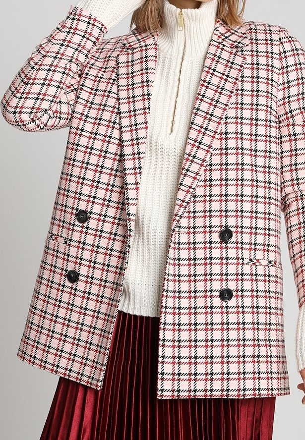 Blazer a doppio petto a quadri in bianco, rosso e nero, con grandi bottoni neri e una vestibilità rilassata, indossato sopra un dolcevita crema e una gonna plissettata.