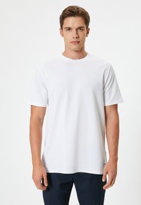 Camiseta de algodón blanca con cuello redondo, mangas cortas y un corte relajado. Sin patrones ni acentos visibles. Diseño liso.